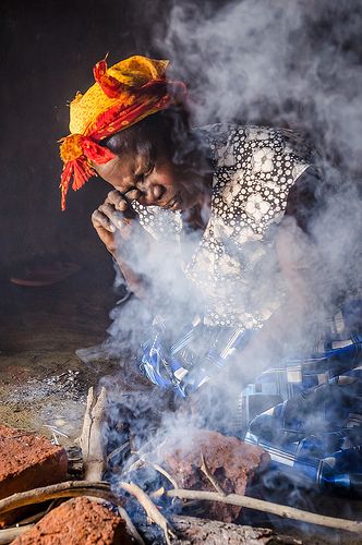 Woman cooking with traditional biomass fuel surrounded by harmful smoke